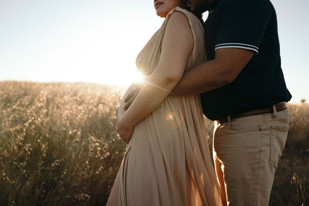 Silhouetted figures embracing in a golden wheat field at sunset with warm backlit glow.