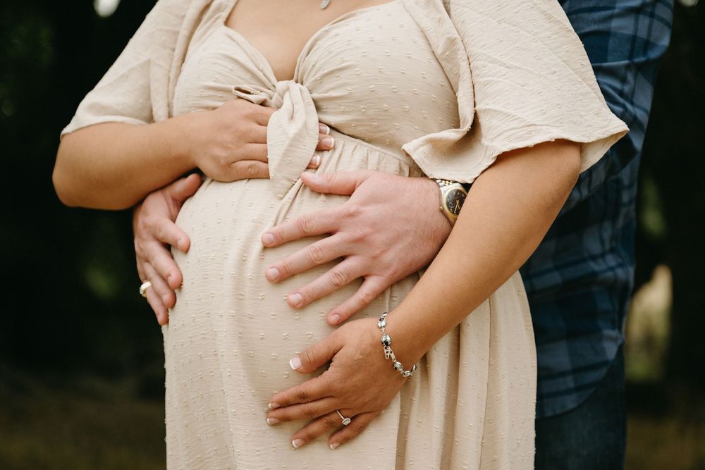 Close-up of hands resting on a pregnant belly wearing a cream-colored maternity dress.