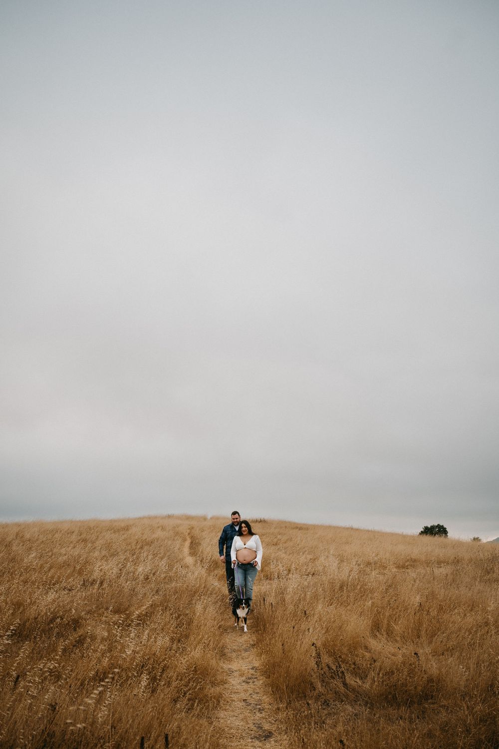 A person walking along a dirt trail through golden grassland under an overcast sky.