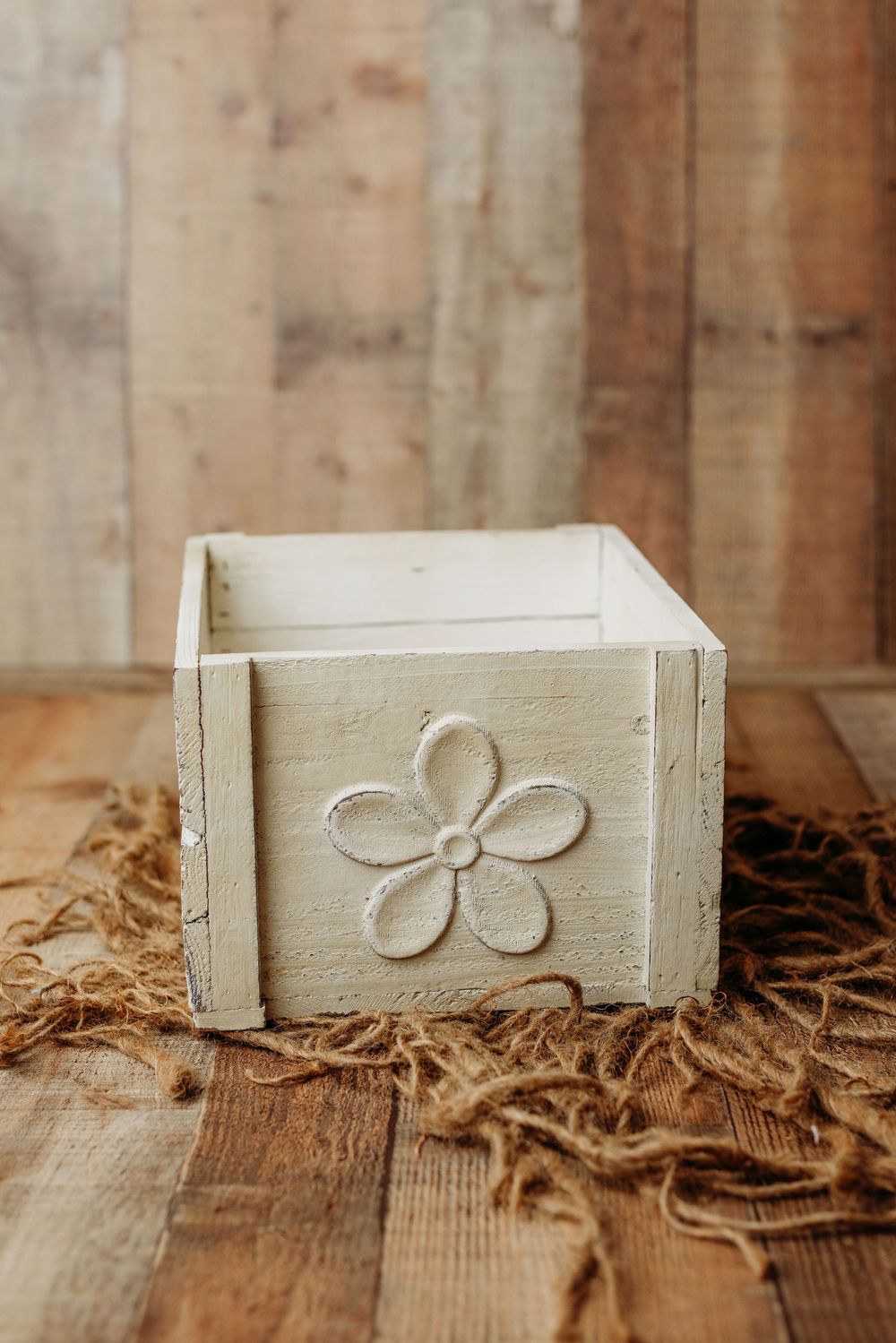 Small white wooden box with carved flower design sits on rustic wooden surface with burlap fabric.