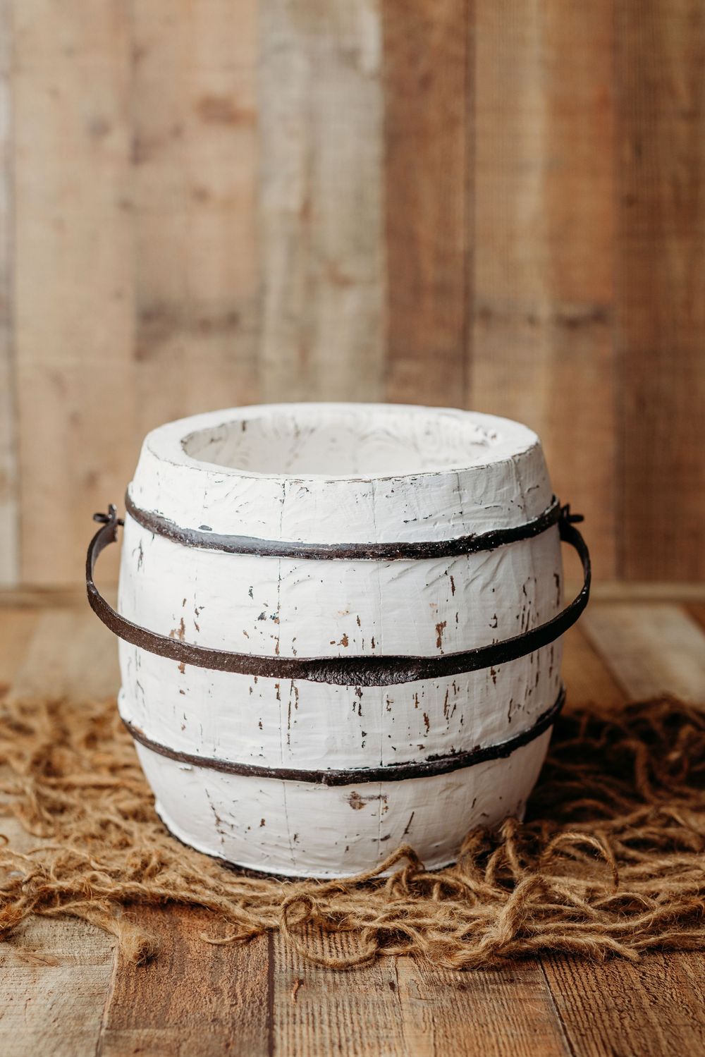 A rustic white ceramic bowl with dark trim sits on a wooden surface with scattered straw or hay underneath.