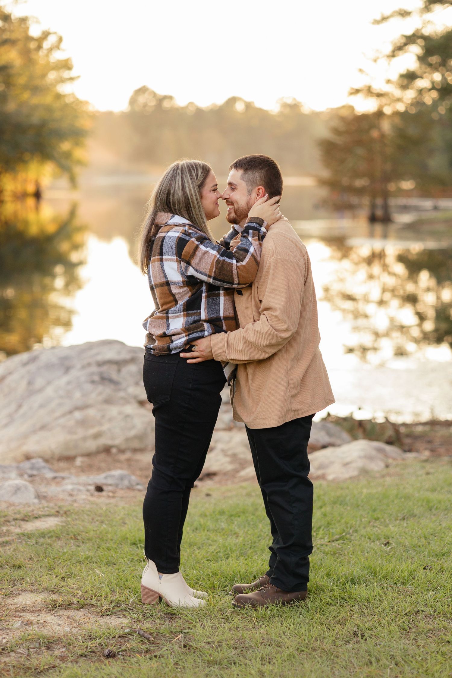 A couple shares an intimate moment at sunset by a lake with golden light filtering through trees.