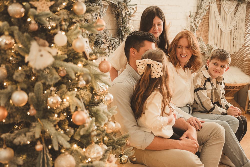 Family in coordinating holiday outfits posing near a decorated Christmas tree with warm lighting.