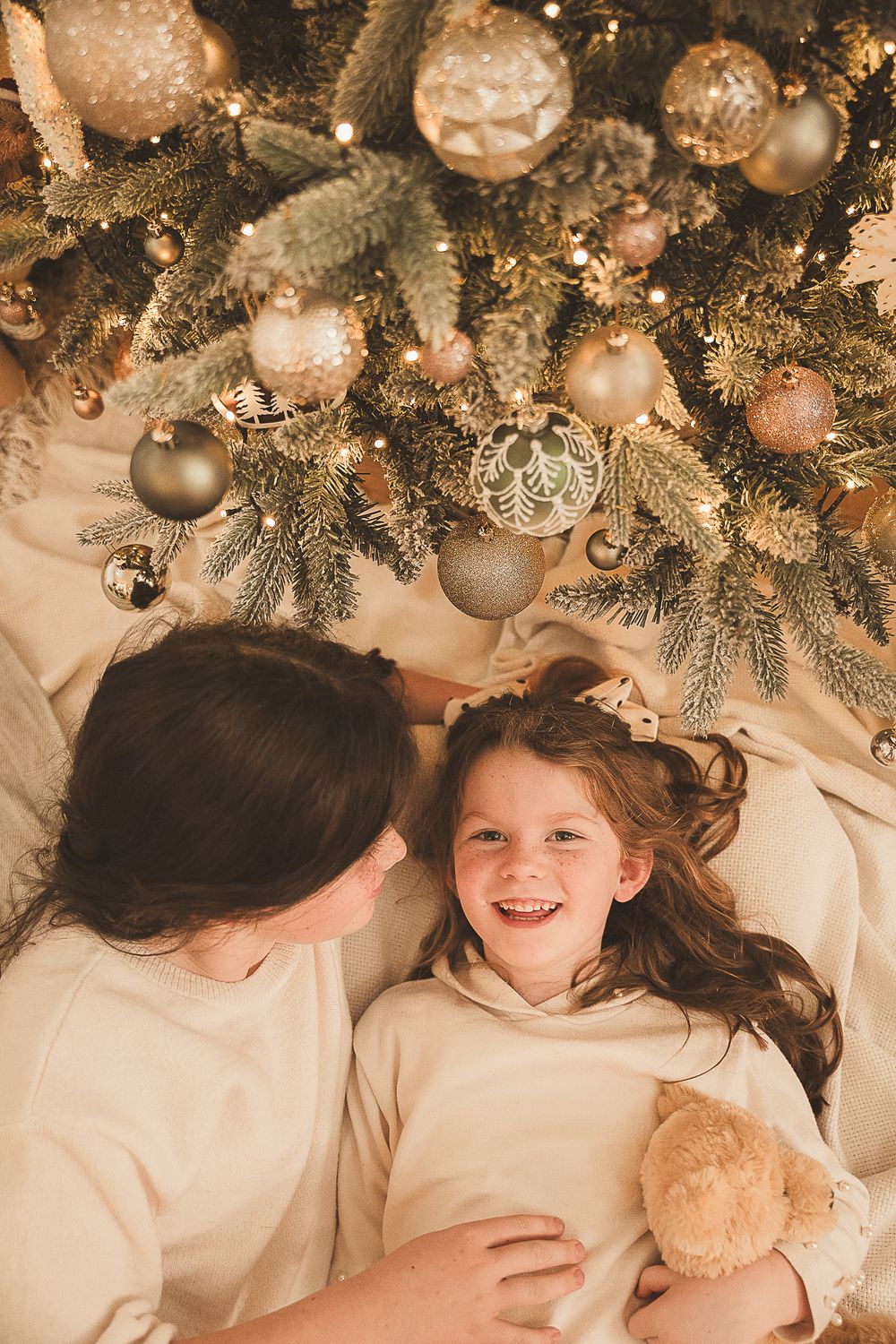 Sweet seasonal portraits captured beneath a decorated Christmas tree with twinkling lights and ornaments.