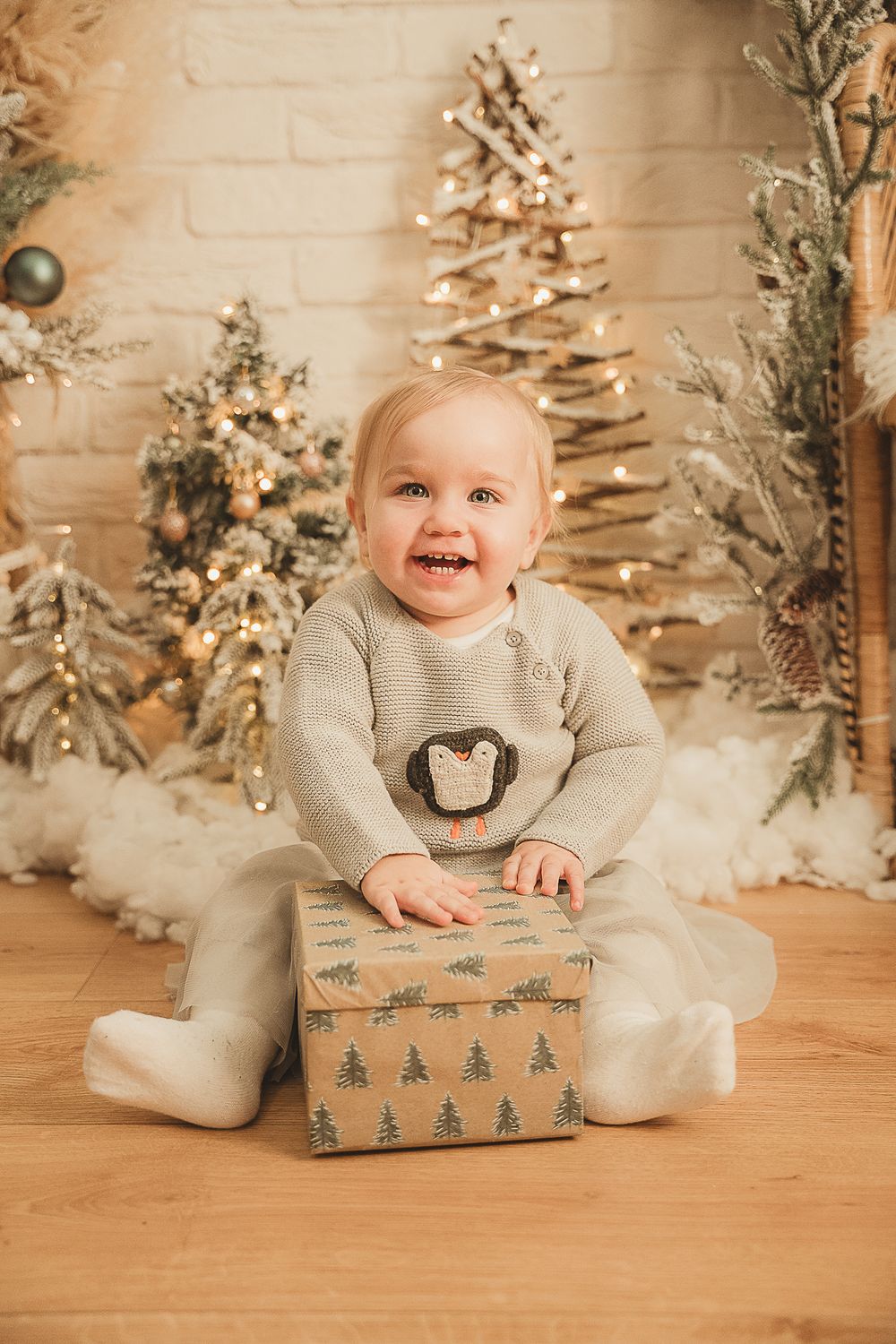 A series of holiday photos showing a young child on a wooden floor with wrapped Christmas gifts and snowy trees.
