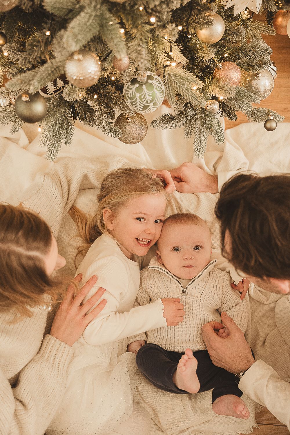 Cozy holiday scene under a Christmas tree decorated with silver and gold ornaments, all wearing cream knit sweaters.