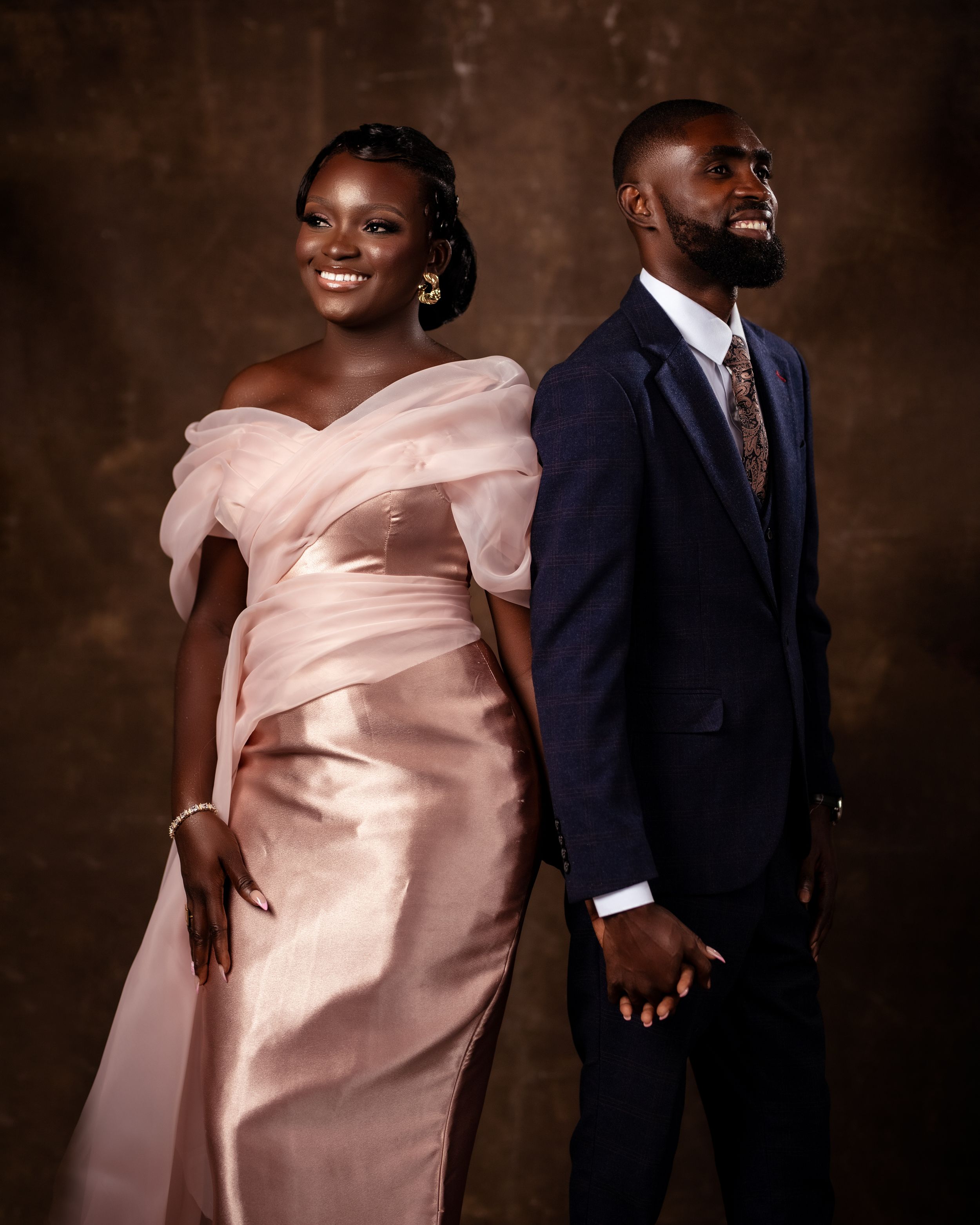 Smiling couple in formal attire; bride in a shimmering champagne gown and groom in a tailored navy suit.