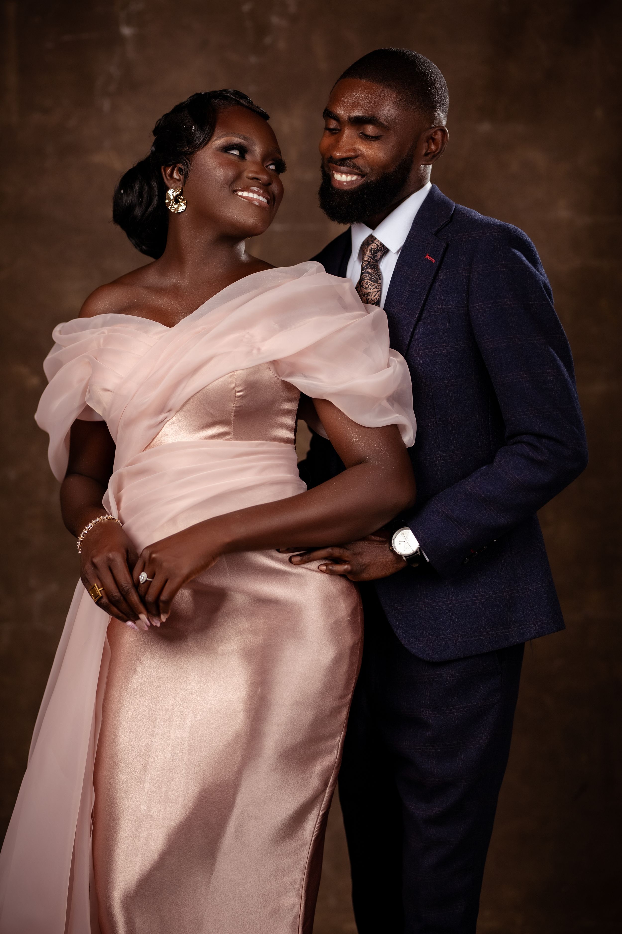 Full-length portrait of a couple in elegant evening wear; woman in champagne pink and man in navy blue.