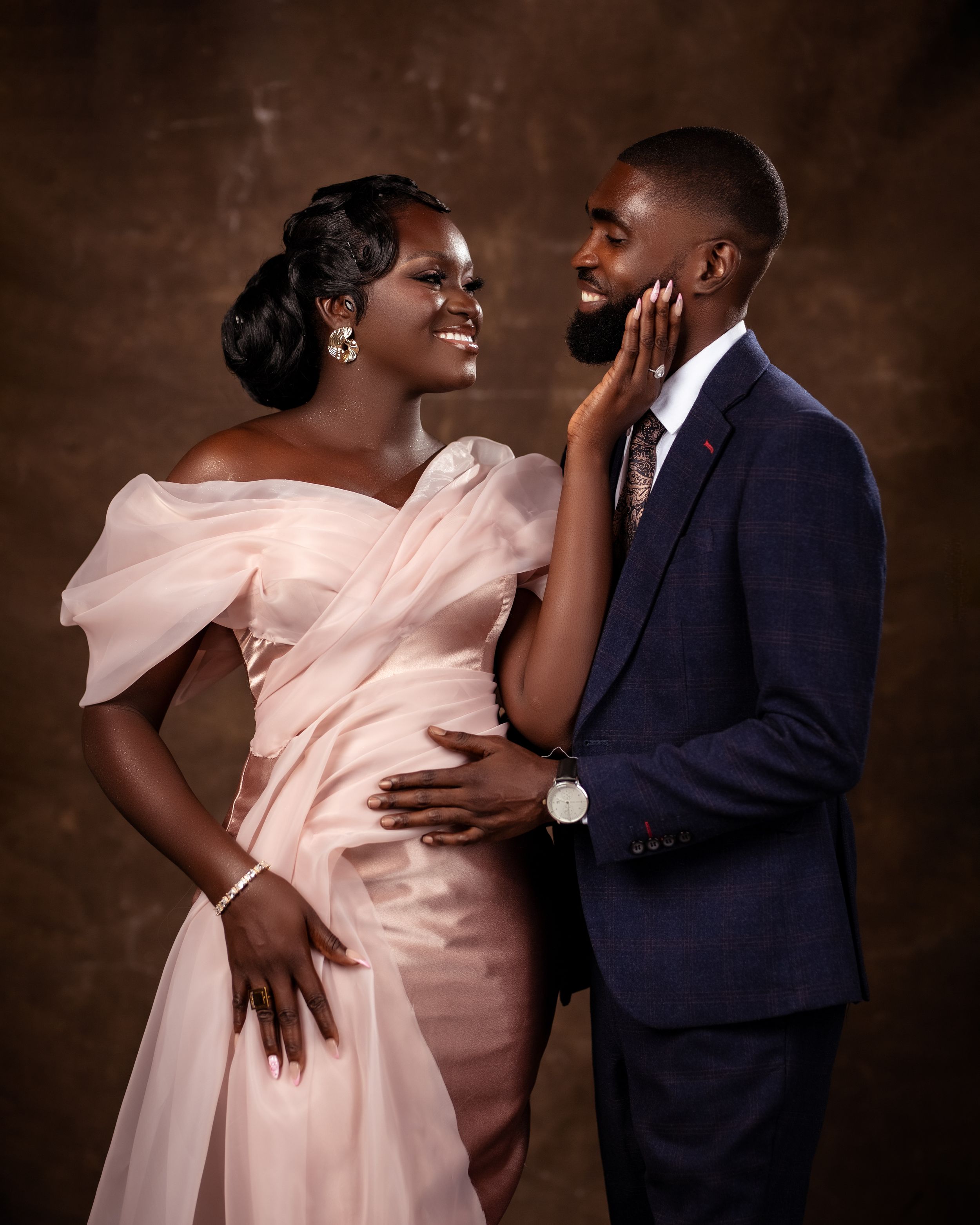 Studio photo of a man in a suit touching his bride's face as they smile together in formal wear.