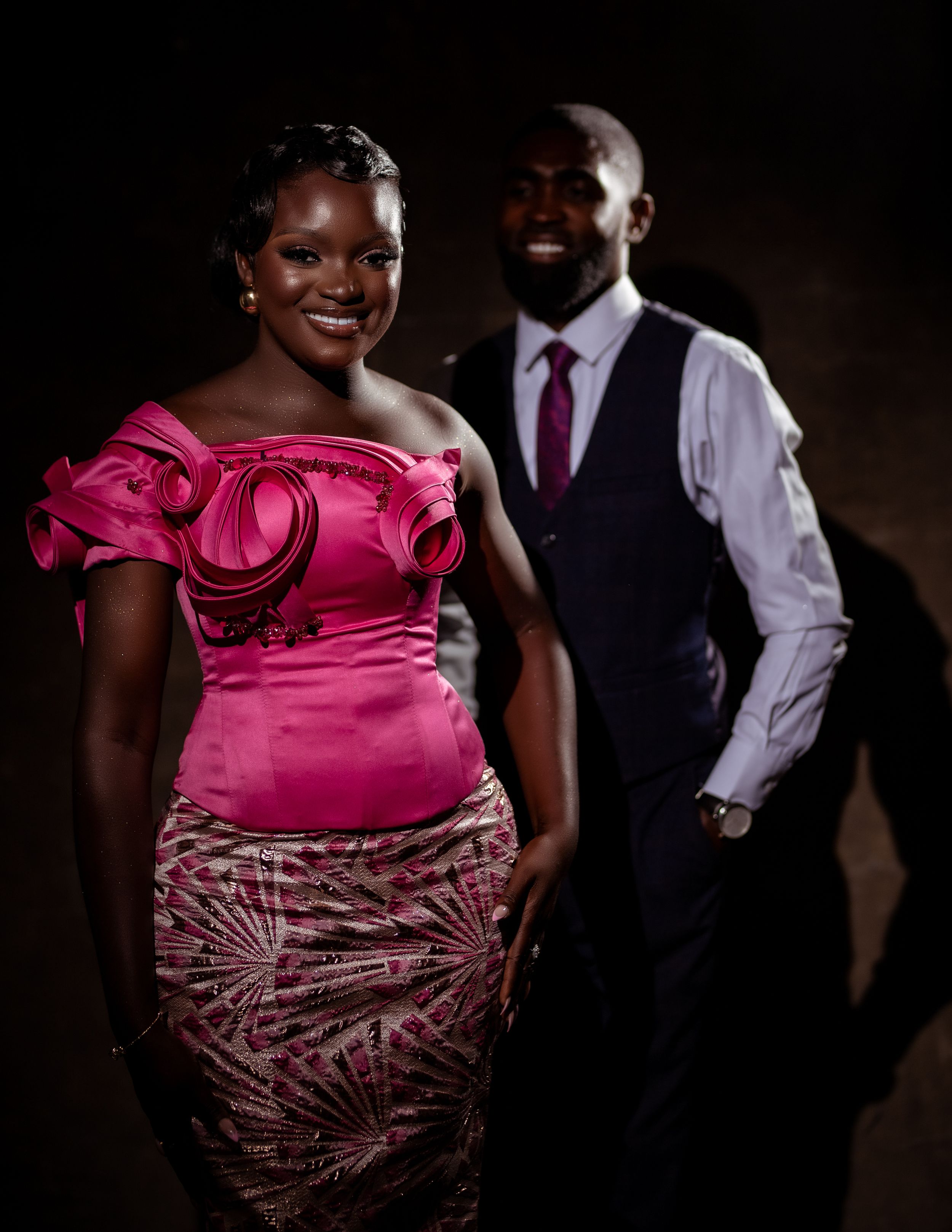 Studio portrait of a couple in formal wear; bride in a pink gown and groom in a navy suit and red tie.