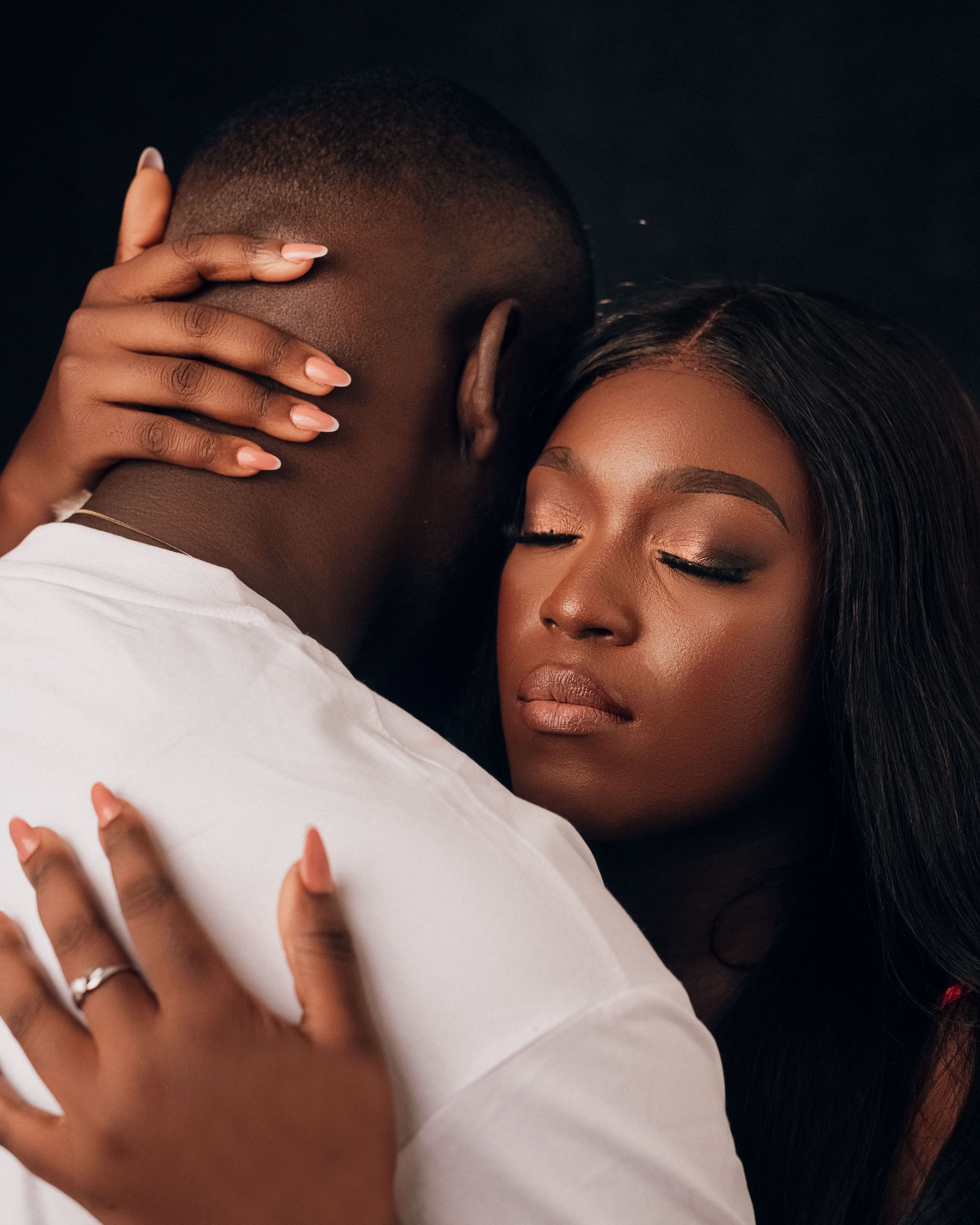 Warm, intimate studio portrait of a couple with the woman leaning her head on the man's shoulder.