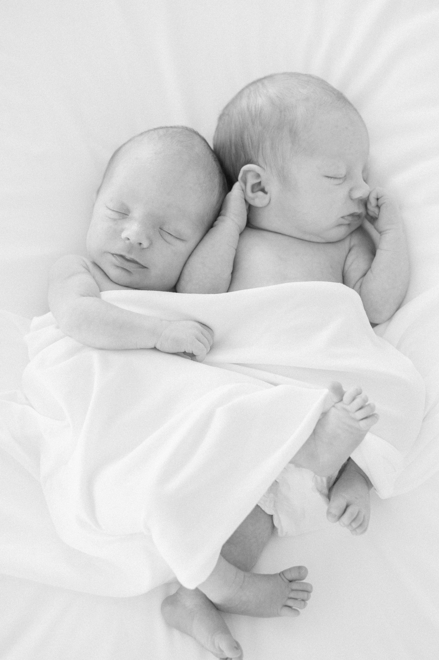 black and white image of baby boys sleeping together and naturally posed, cuddling up together