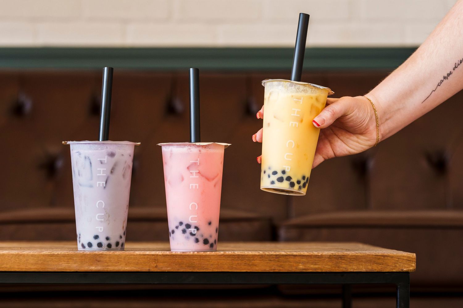 Three colorful bubble tea drinks with tapioca pearls served on a wooden surface.