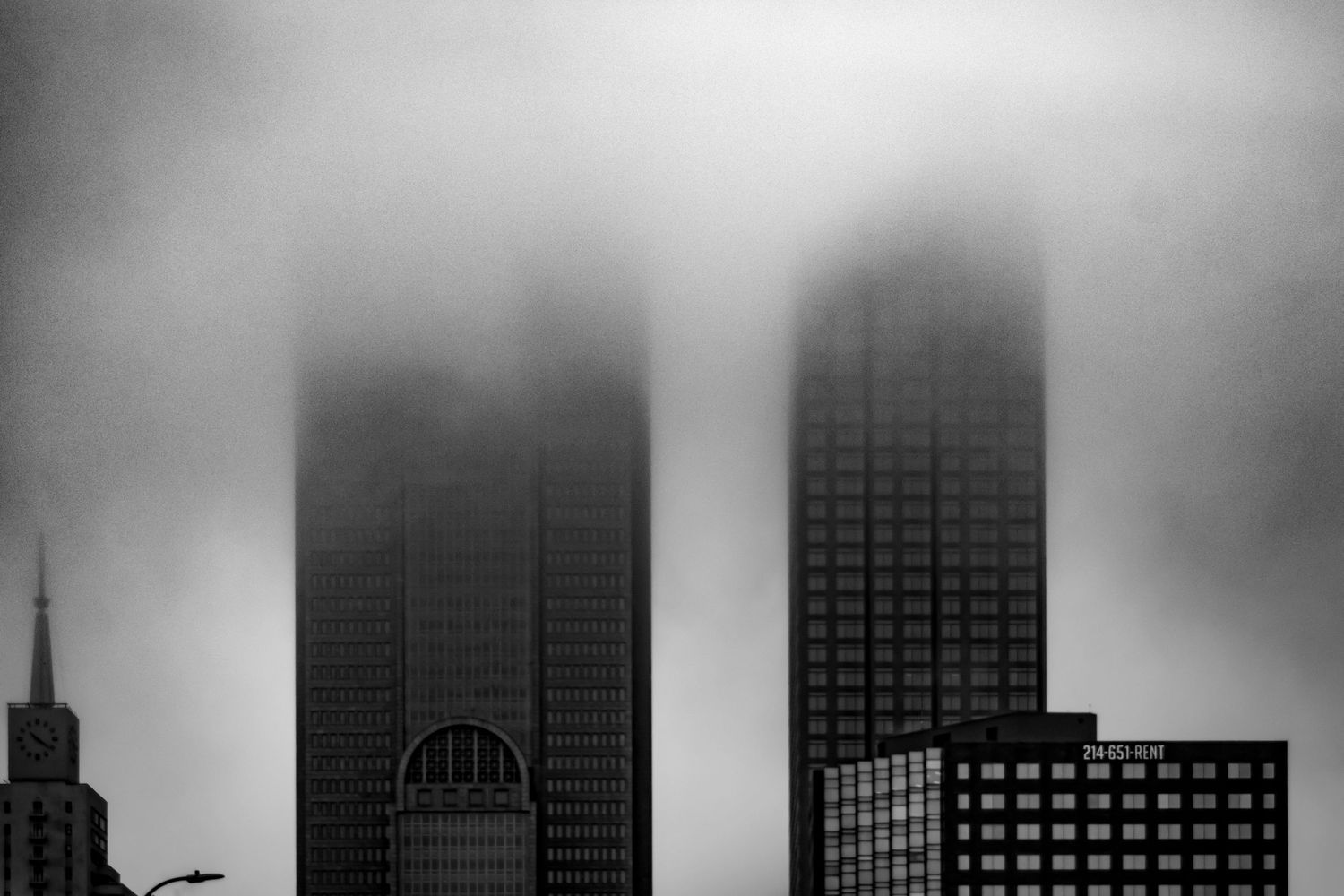 Foggy cityscape with skyscrapers disappearing into dark moody clouds in black and white.