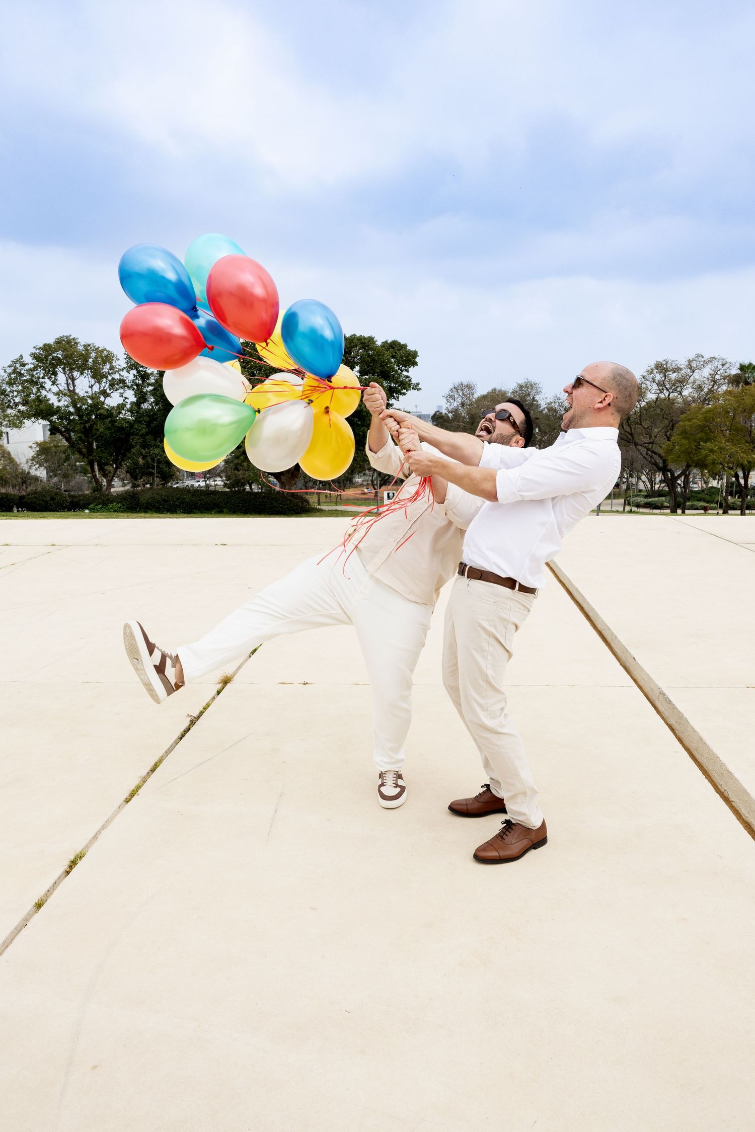 Groom and Groom celebrating and laughing while holding a big bouquet of ballons before their Tel Aviv Wedding at the Dubnov Gallery