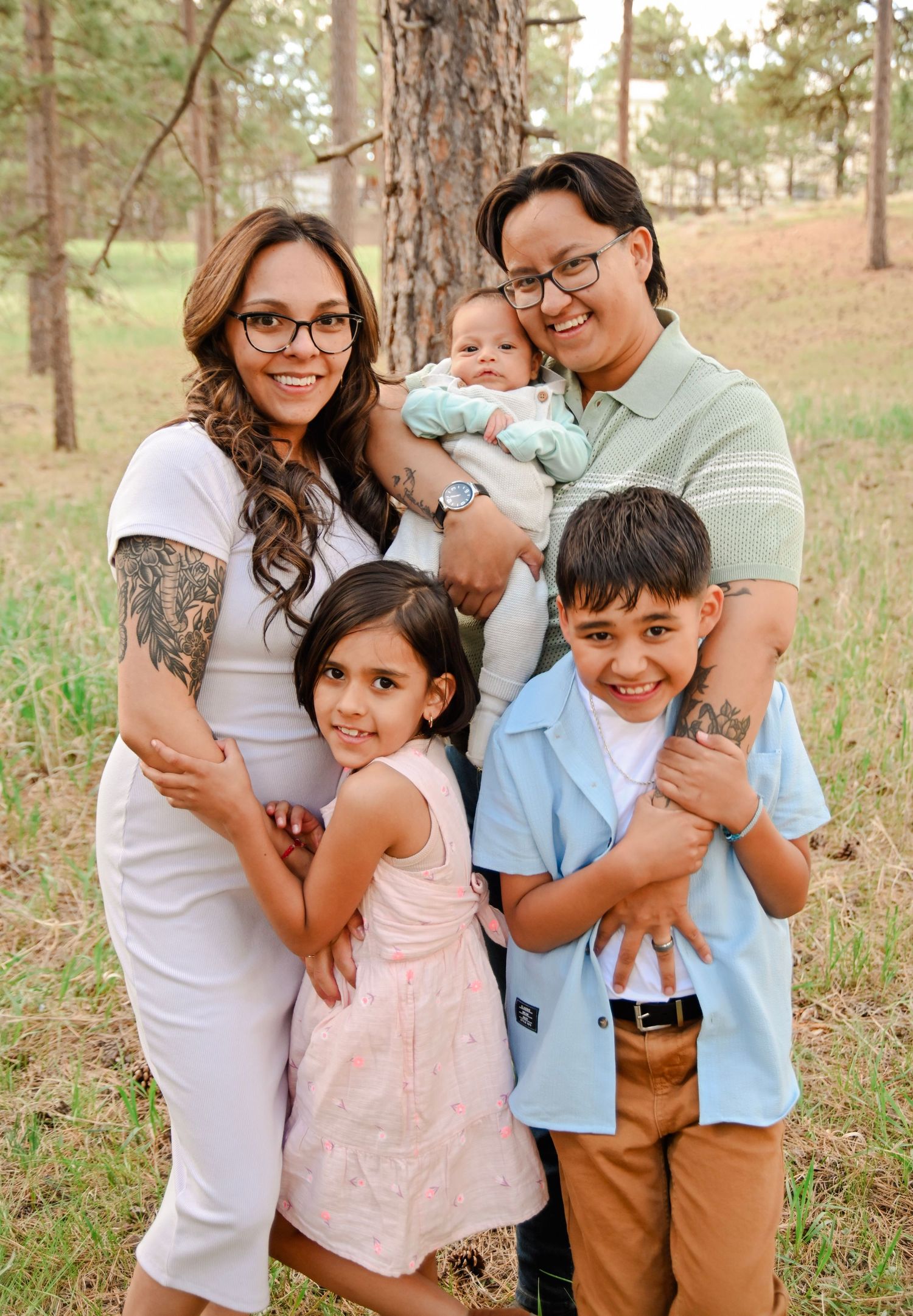 Happy family with three young children standing together outdoors in a pine forest setting for a portrait.