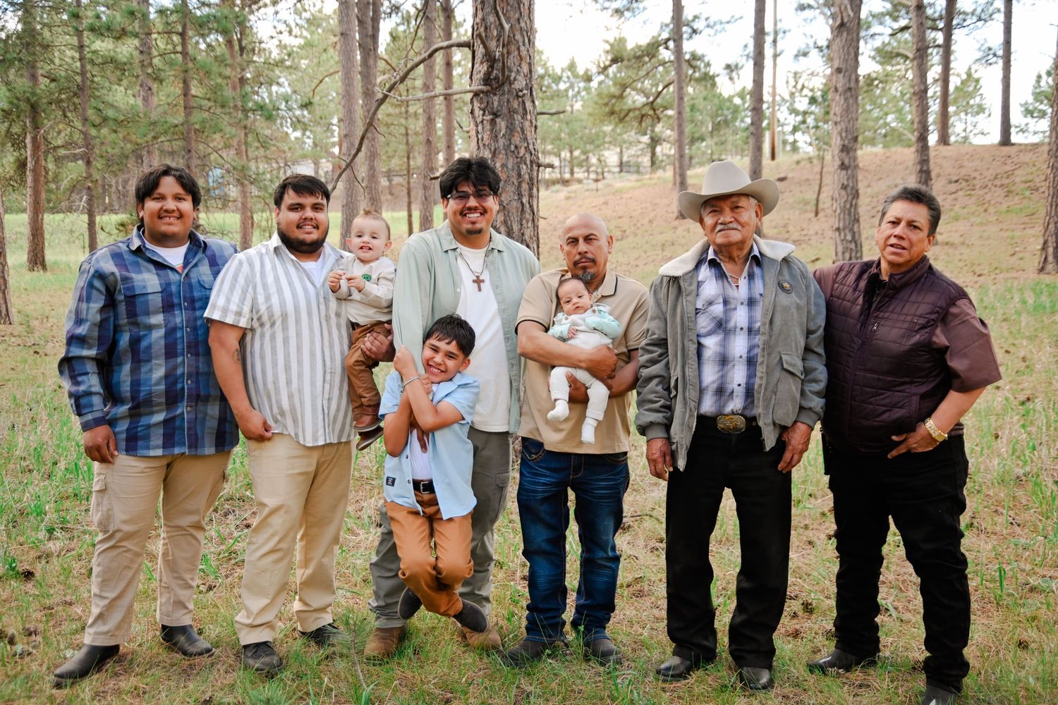 A group of people pose together in a line against pine trees in a forest setting.