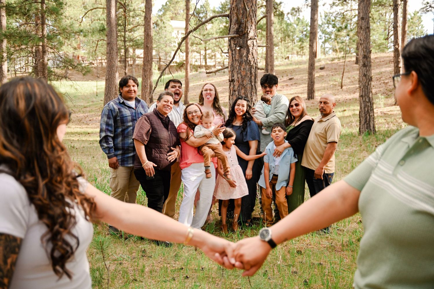 A group enjoys a fun outdoor celebration in a sunny forest clearing while holding hands in a circle.