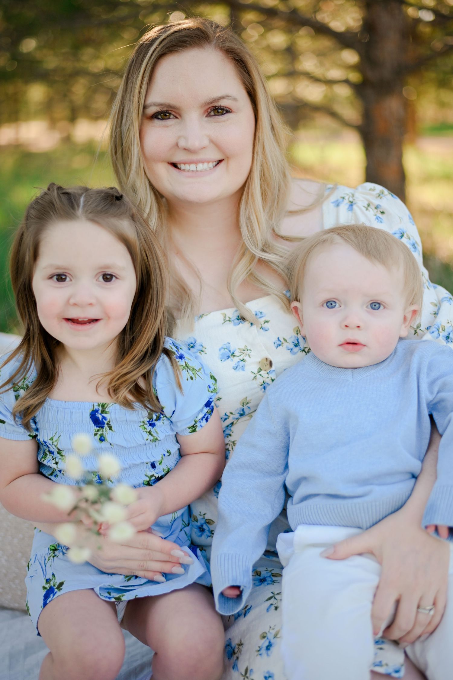 Family portrait with coordinating blue and floral outfits sitting together in an outdoor garden setting.
