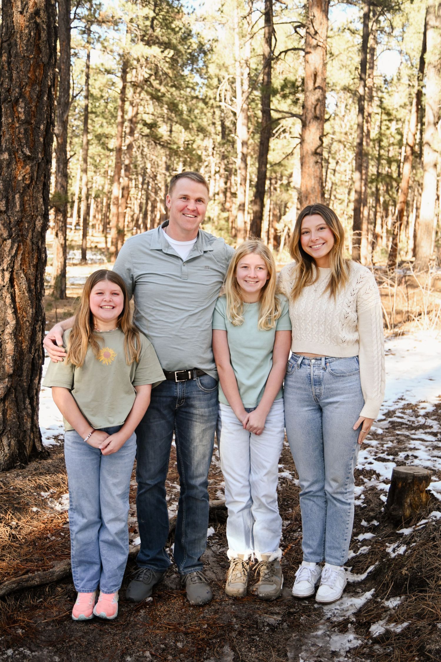 A group stands together in a snowy pine forest on a winter day wearing casual clothing.