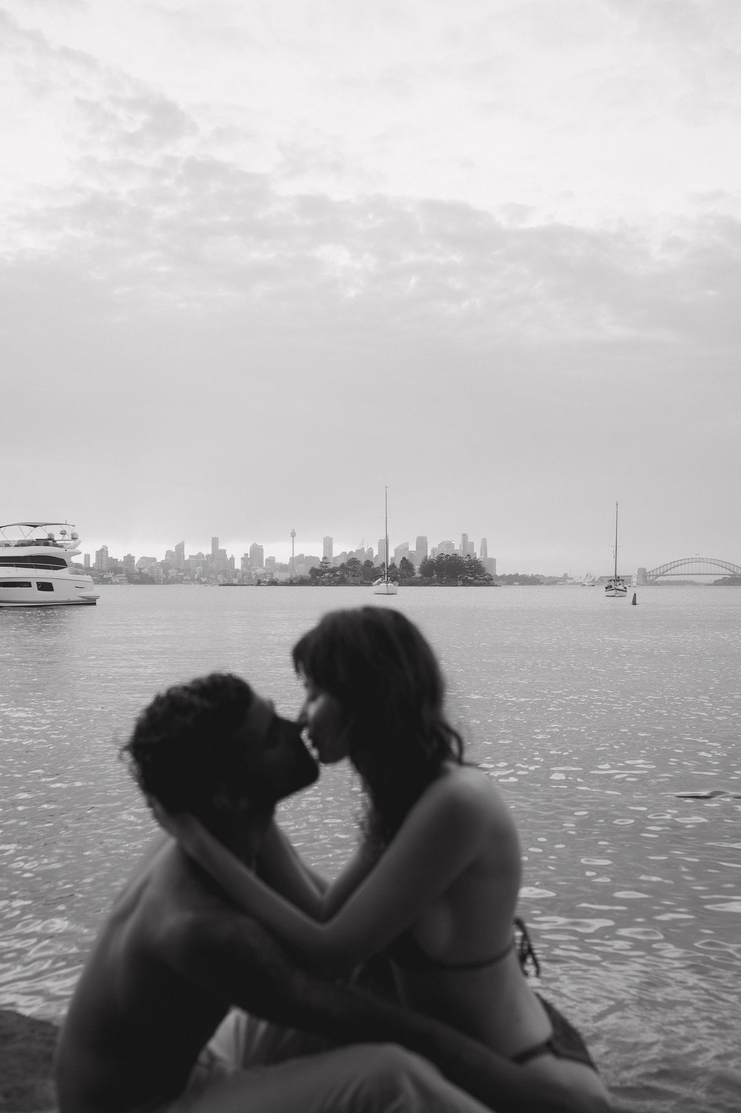 Silhouettes against water with city skyline and boats in background.