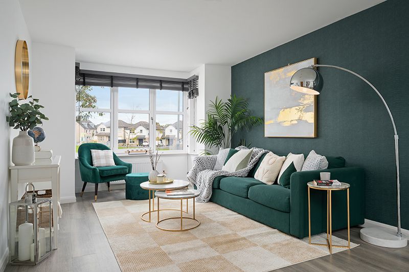 Modern living room interior with emerald green accent wall, white furniture, and gold decor elements.