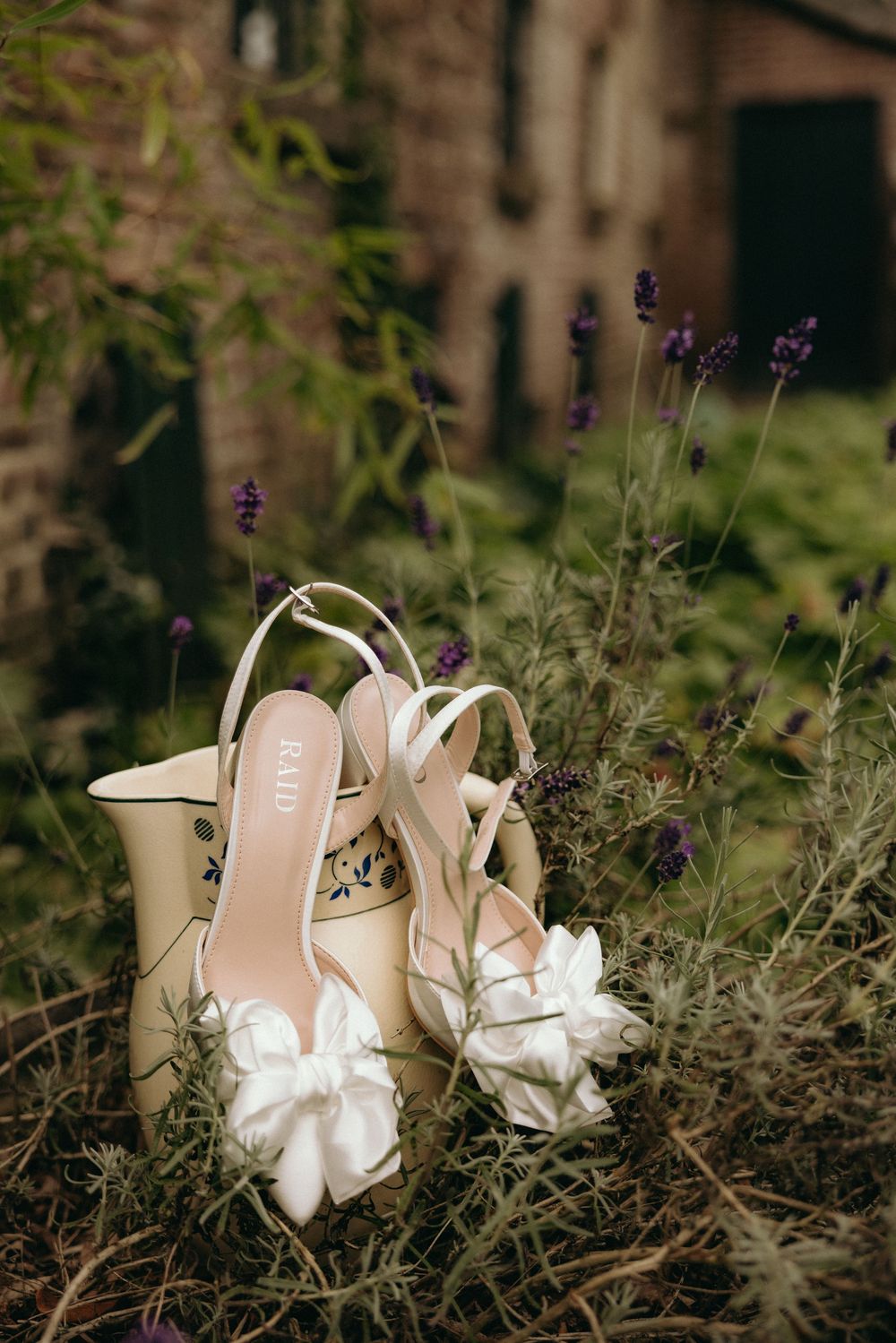 Elegant cream bridal shoes with bow details displayed among purple wildflowers.