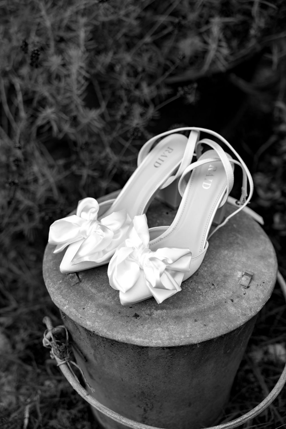 White bridal shoes with bows displayed on a dark concrete surface in an artistic black and white composition.