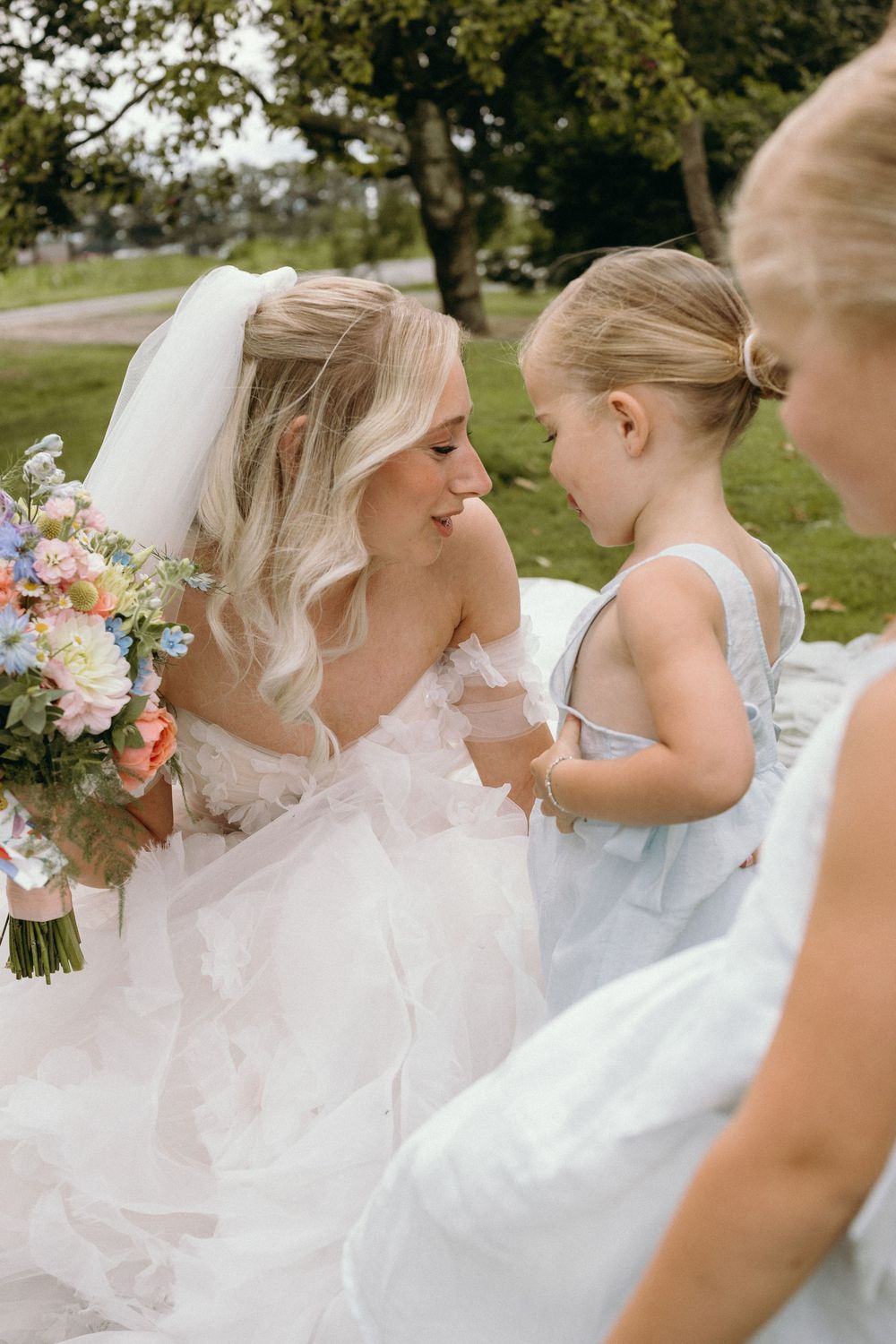 Bridesmaids in light blue dresses sharing joyful moments with the bride in a garden setting.