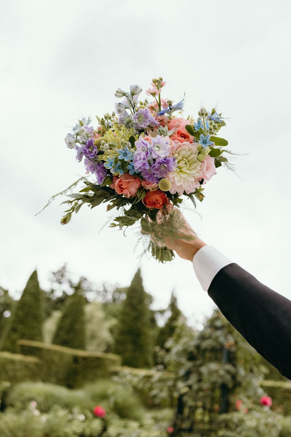 Colorful wedding bouquet with purple, pink and yellow flowers held up against bright sky.