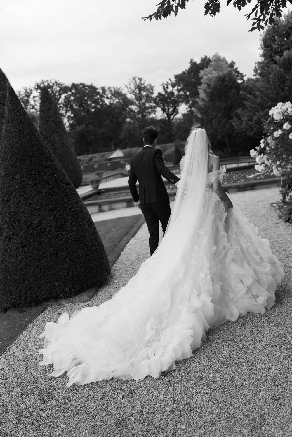 A bride's dramatic wedding dress train flows across a gravel path during an outdoor photoshoot.