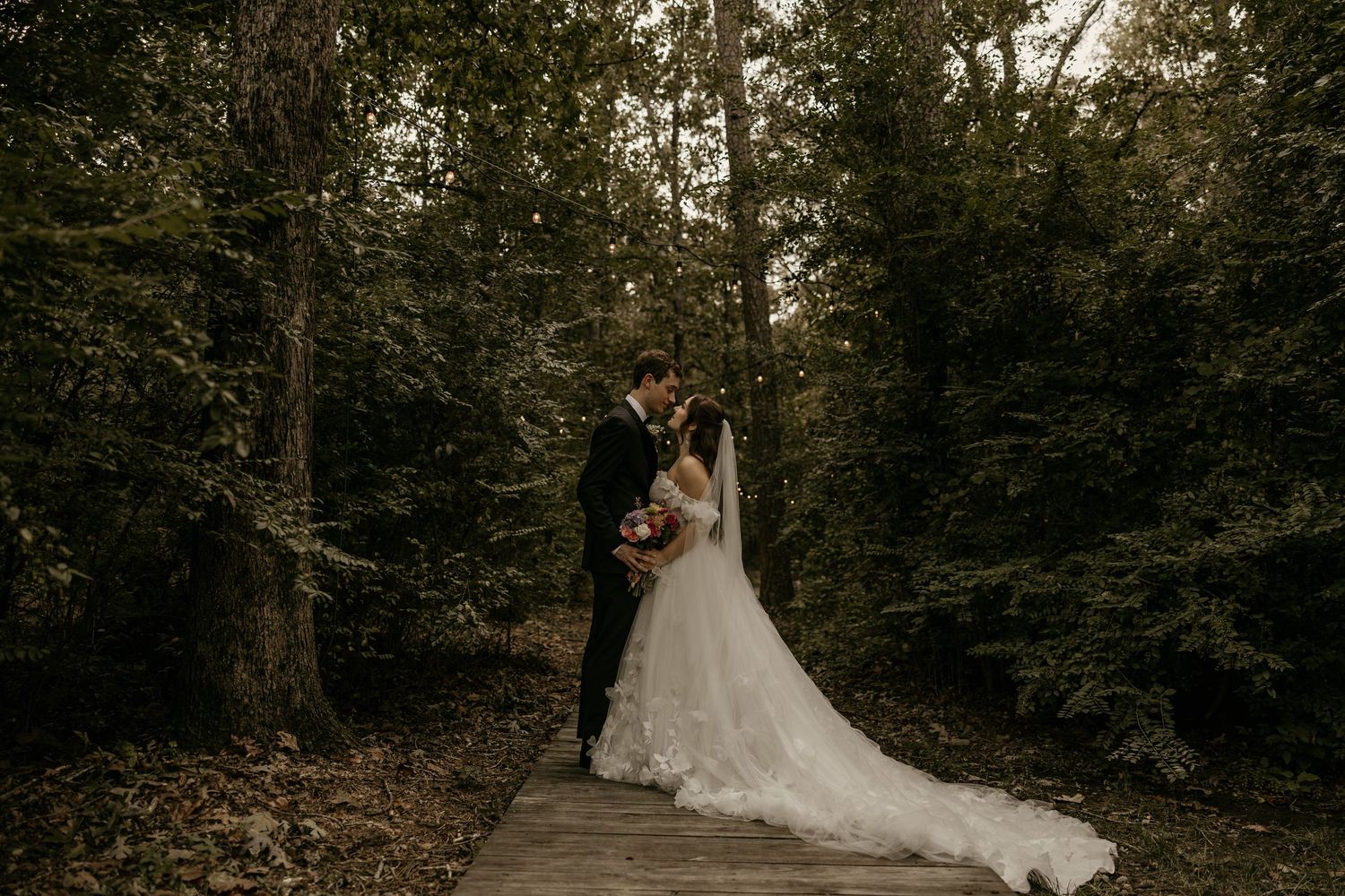 A beautiful bride poses on a wooden boardwalk with a floral bouquet and flowing veil.