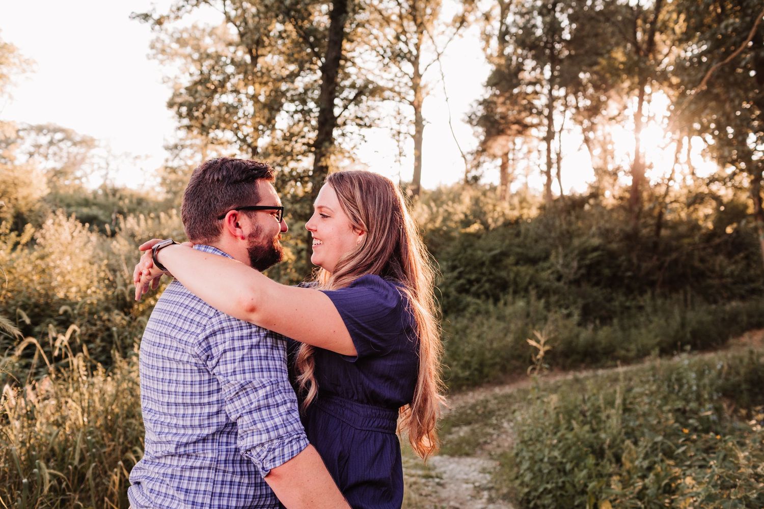 Couple embracing and smiling at each other in a sunlit forest clearing during golden hour.