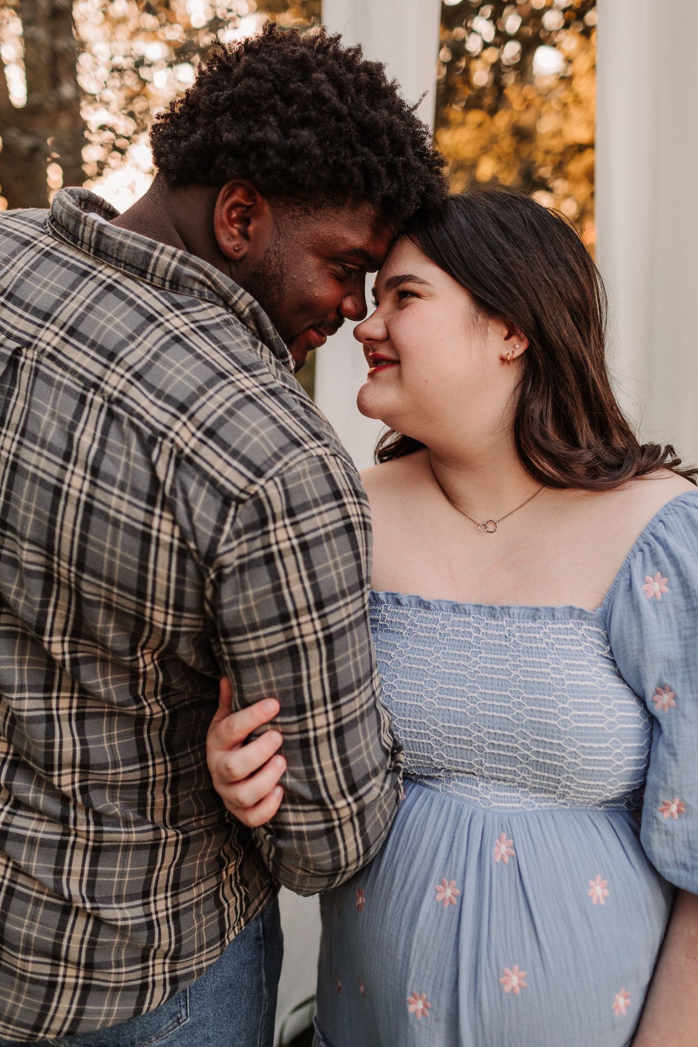 Couple sharing a tender forehead-to-forehead moment, woman in blue floral maternity dress smiling.