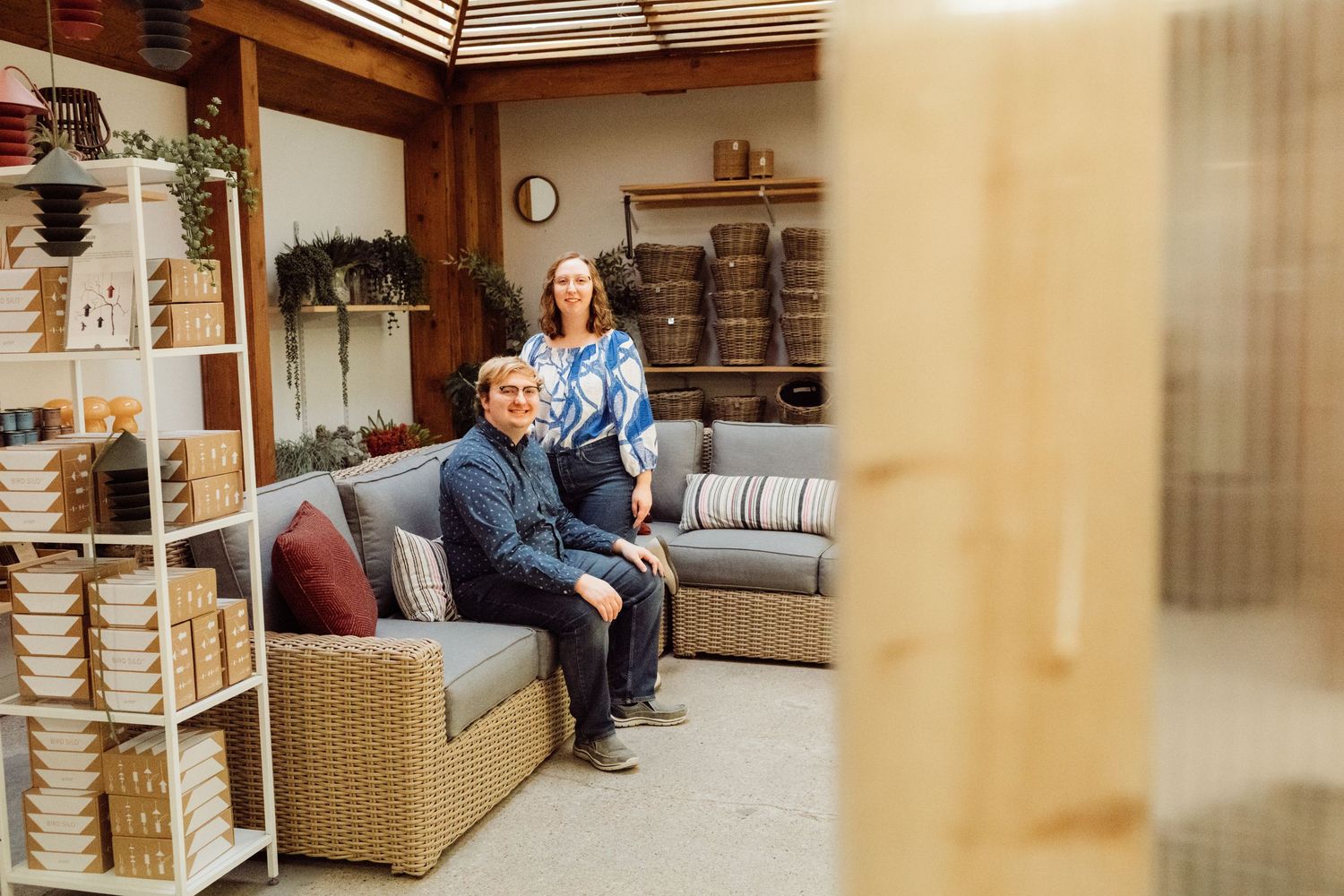 Couple posing in a cozy outdoor furniture display area surrounded by shelves of woven baskets.