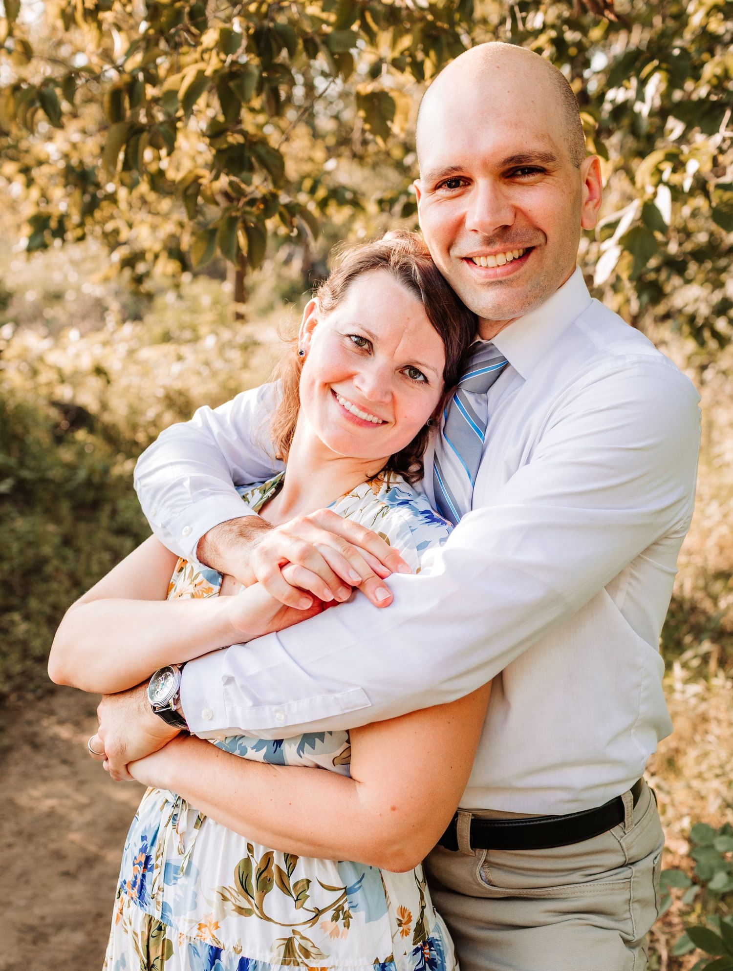 Happy couple embracing and smiling together in a sun-dappled outdoor setting.