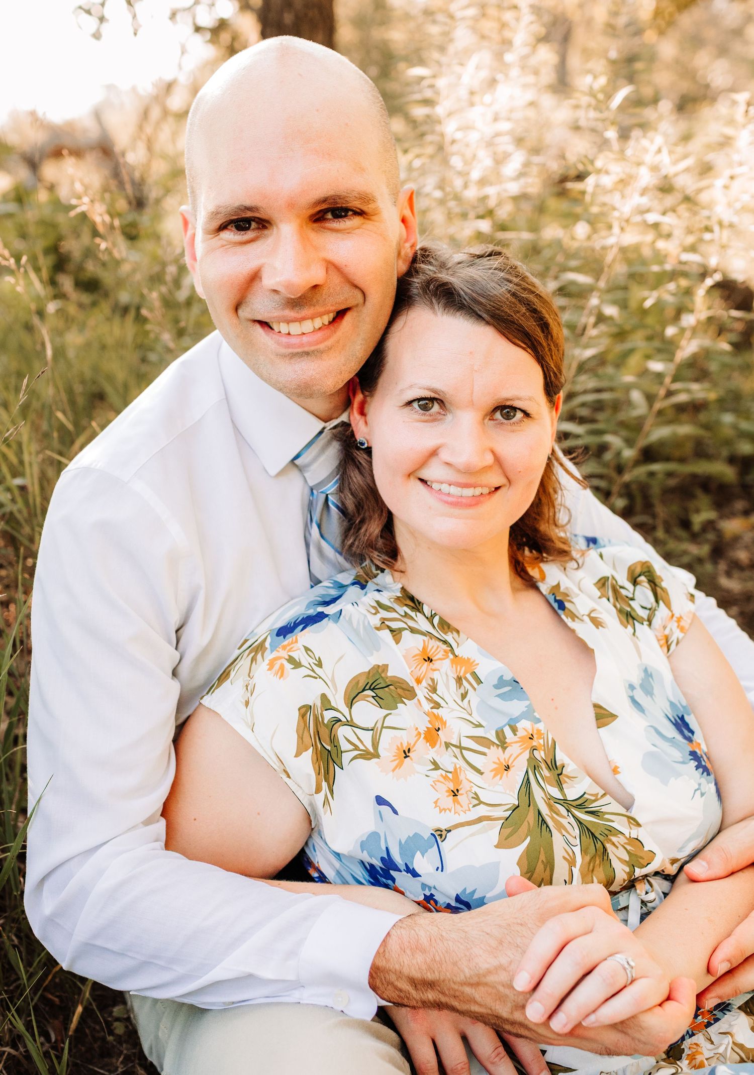 Smiling couple sitting closely together in a warm sunlit outdoor family portrait.