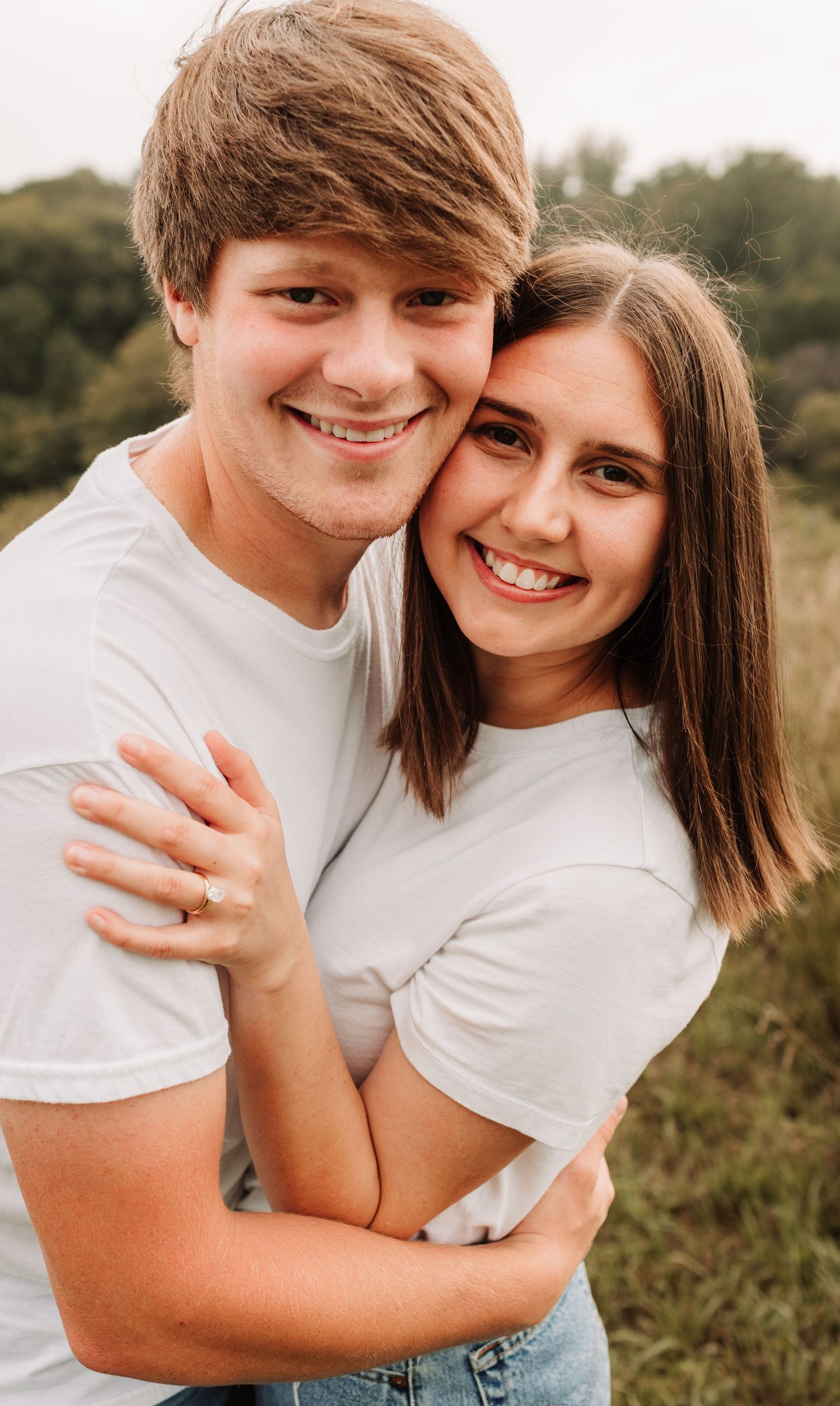 Smiling young couple in matching white t-shirts embracing in an outdoor field setting.