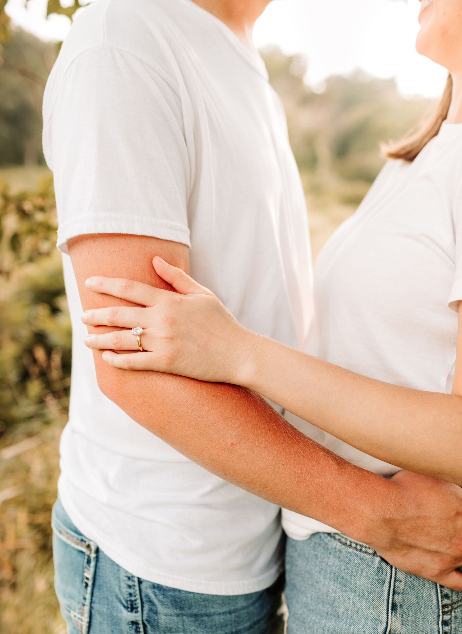 Close-up of a couple embracing outdoors, woman's hand with engagement ring wrapped around man's arm.