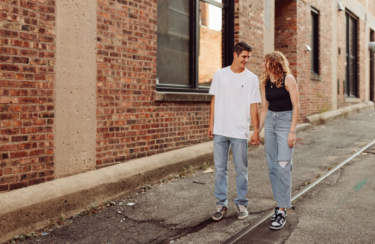 Young couple walking and laughing together in an urban alley with brick walls and casual style.