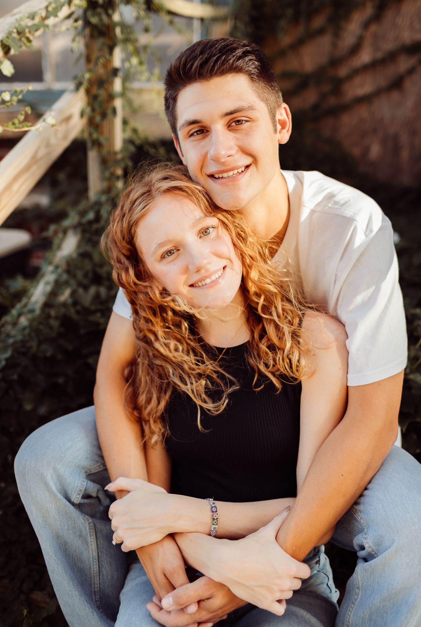 Young couple smiling and embracing outdoors, man hugging woman from behind in warm golden light.