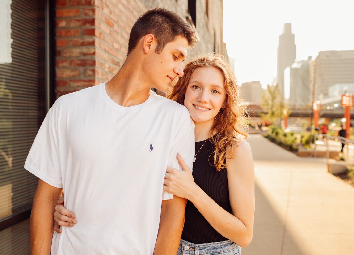 Happy young couple in casual outfits walking together near brick wall in urban setting.