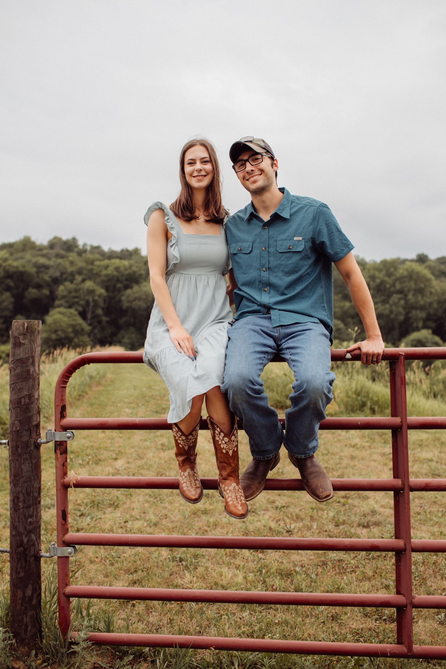 Smiling couple sitting together on a rustic red farm gate in a rural field.