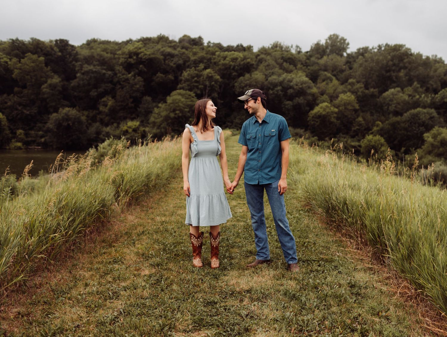 Couple holding hands and gazing at each other in a lush green meadow.