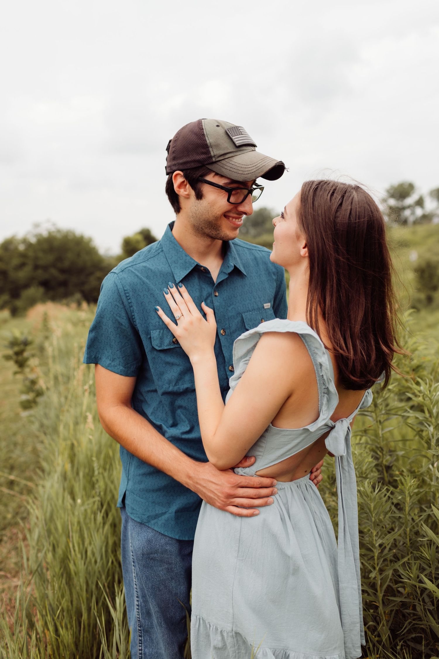 Young couple embracing and smiling at each other in a lush green field during an outdoor engagement photo session.