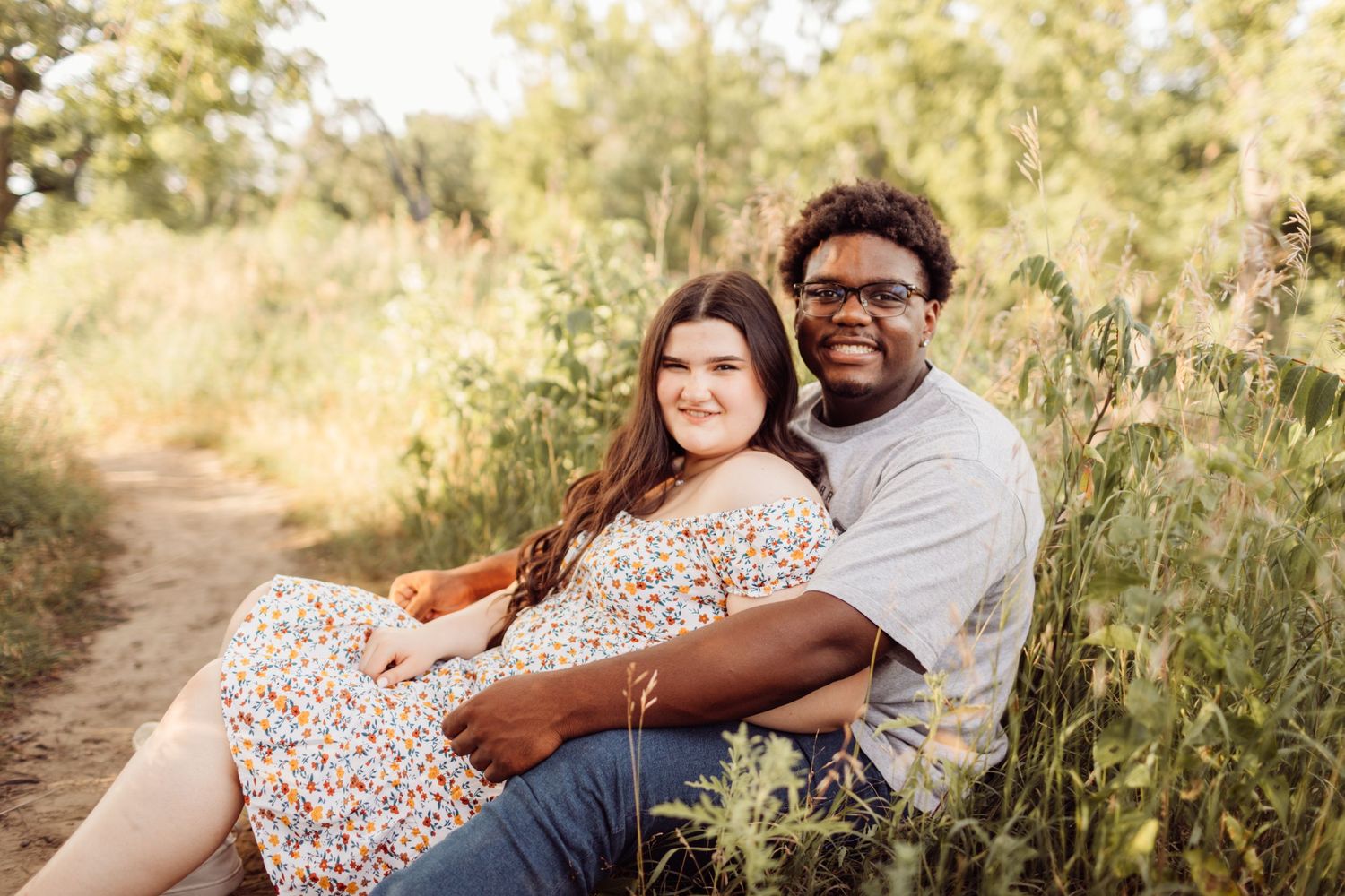 Young couple sitting together on a dirt path surrounded by lush greenery.