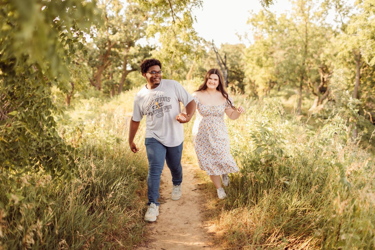 Couple running hand in hand along a sunlit nature trail.