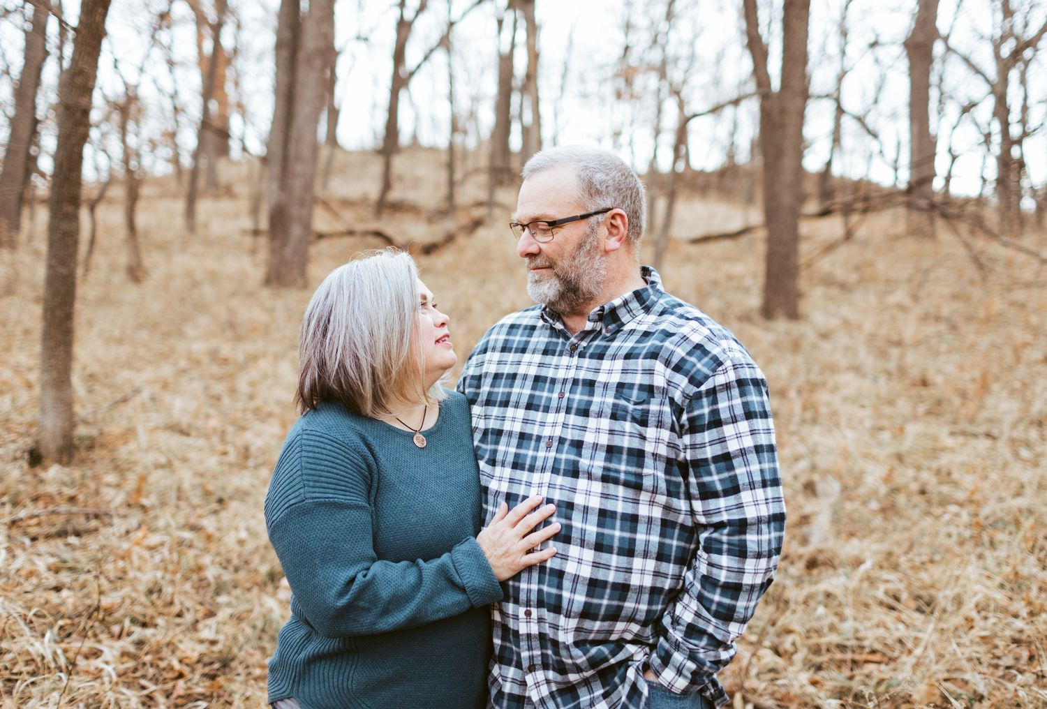 Couple sharing a joyful moment in an autumn forest, smiling at each other warmly.