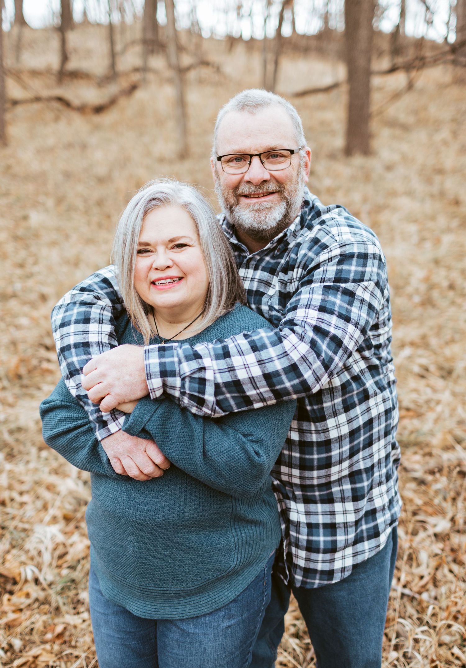 Happy couple hugging in a fall woodland setting, man in plaid shirt embracing smiling woman.