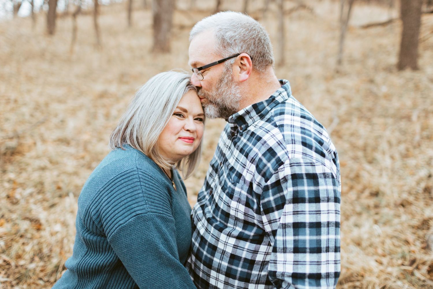 Older couple sharing an intimate moment in autumn woods, man gently kissing woman on forehead.